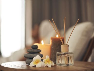 Spa setup with candles, stones, flowers, and reed diffuser on a wooden table.