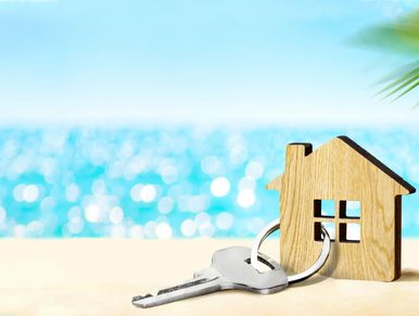 Wooden house keychain with a key on a sandy beach by the sea.