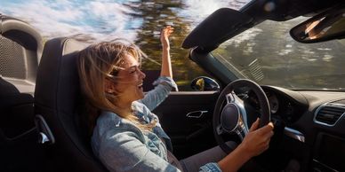 A joyful woman driving a convertible with her hand in the air.