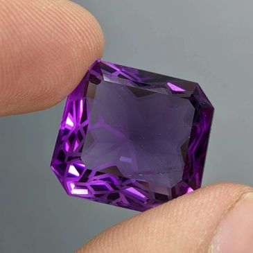 A hand holding a rectangular purple gemstone with intricate facets.