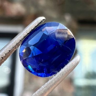 Close-up of a deep blue faceted gemstone held by tweezers.