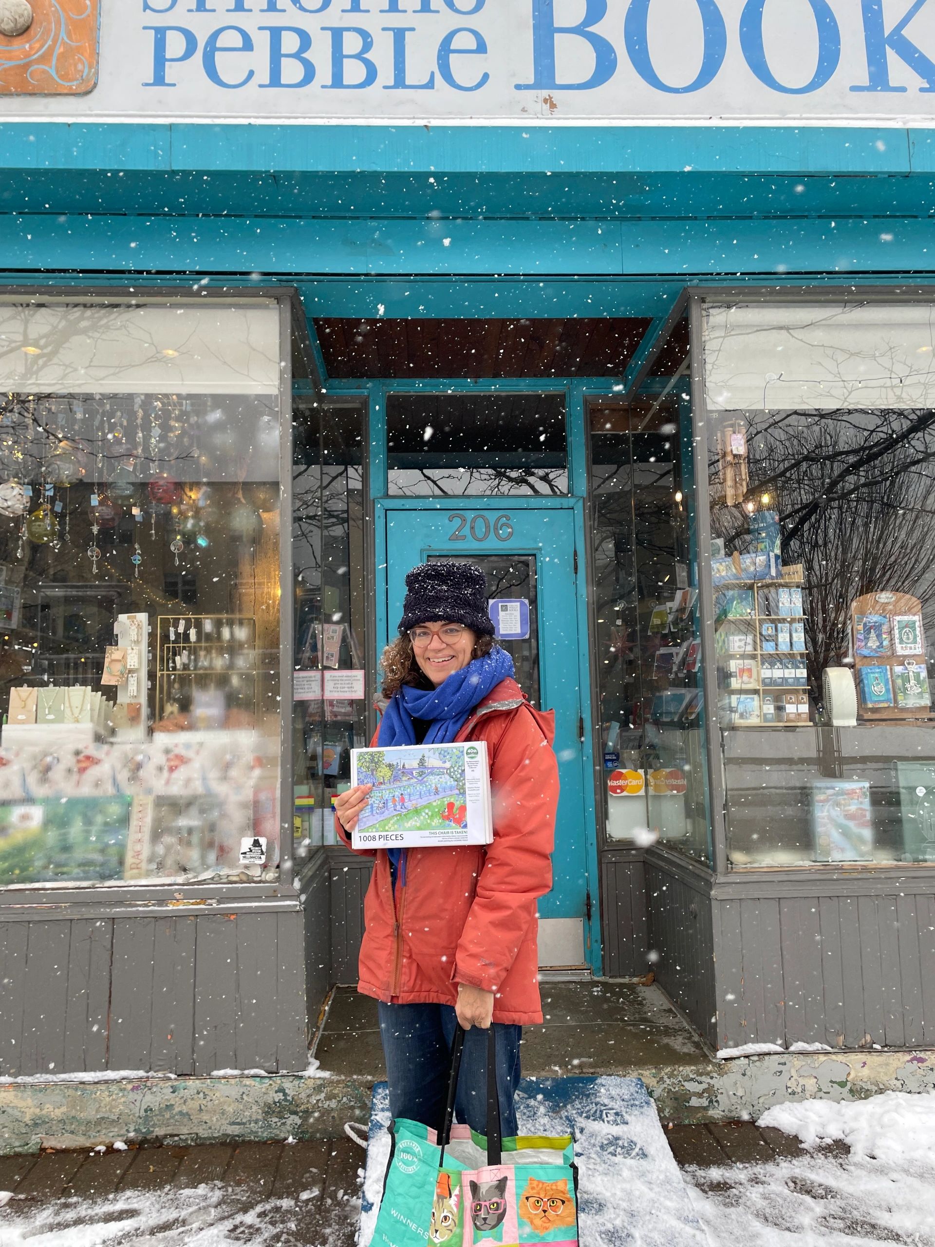Lucianne Poole holds a puzzle of her painting, while standing in front of Singing Pebble Books.