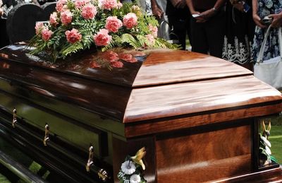 A polished wooden coffin adorned with pink flowers at a funeral.