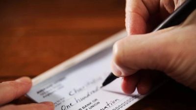 A person writing a check with a pen.