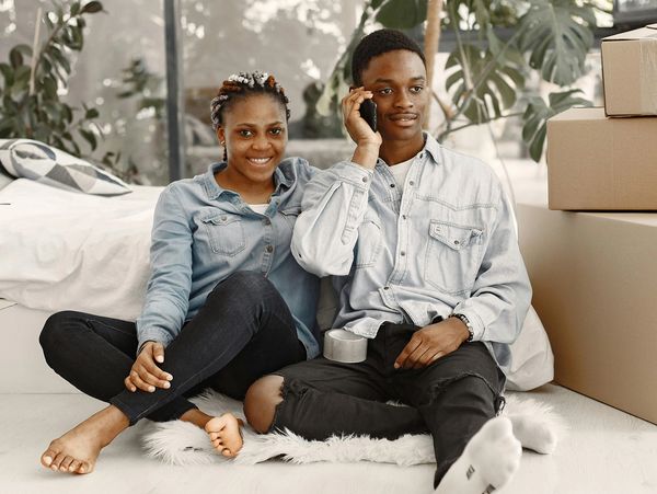 A young couple sitting on the floor surrounded by moving boxes.