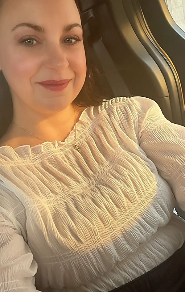 Woman in a white textured blouse smiling warmly in golden light.