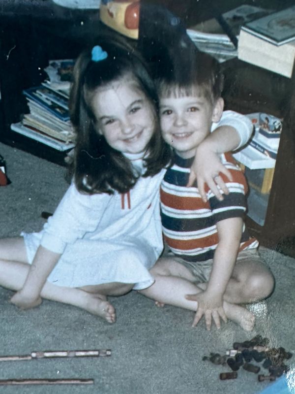 Two kids happily sitting on the carpet, hugging each other.