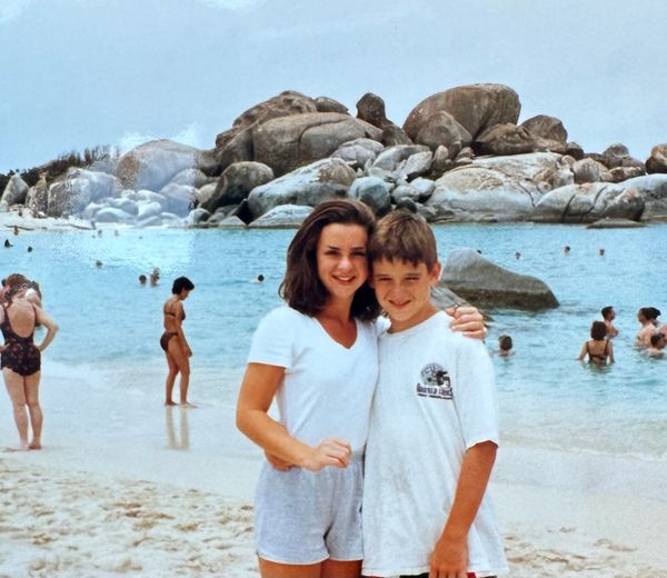 Two kids posing happily at a rocky beach with clear blue water.