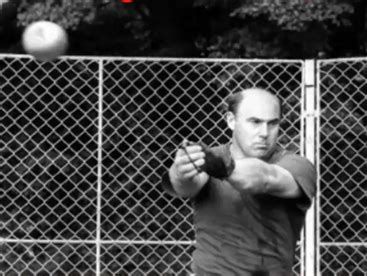 Man focused on throwing a shot put outdoors near a chain-link fence.