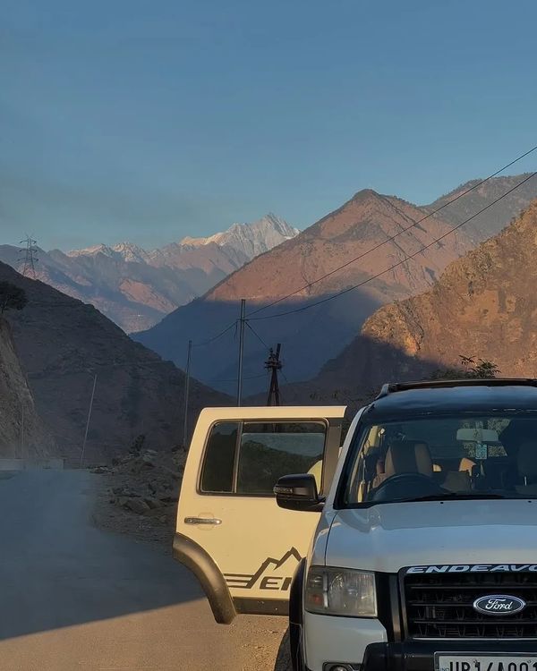 Ford Endeavour on a scenic mountain road during sunrise, with Himalayan peaks in the background 