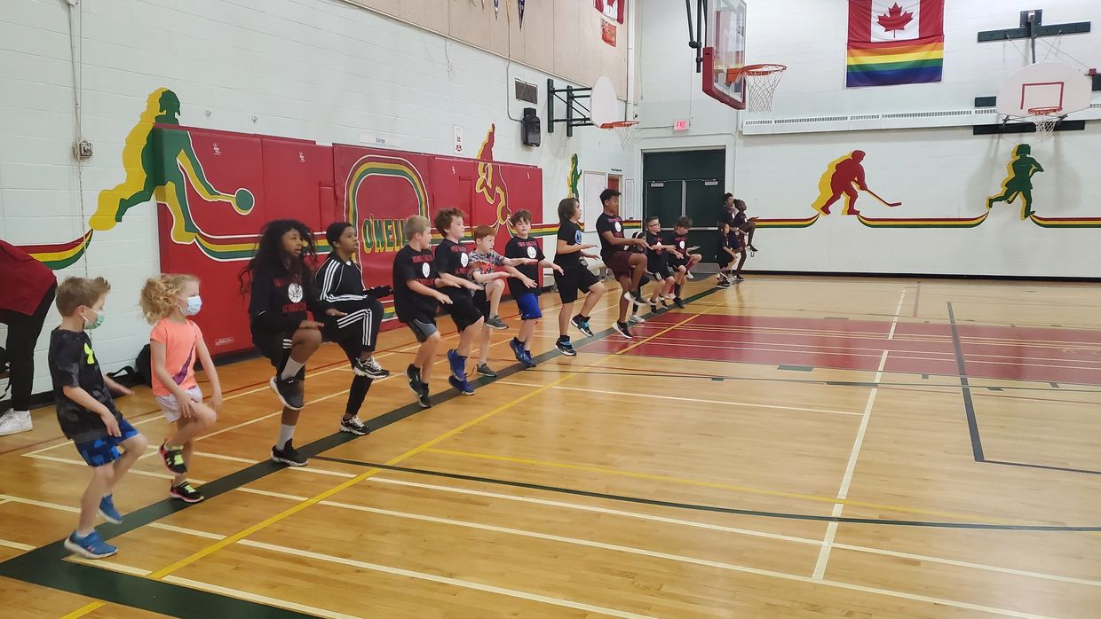 Children lined up in gymnasium practicing balance exercises together.