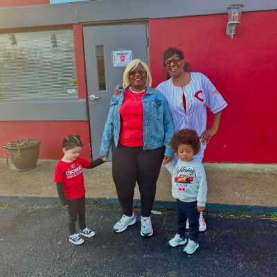 Two women and two children standing outside a red building, holding hands.