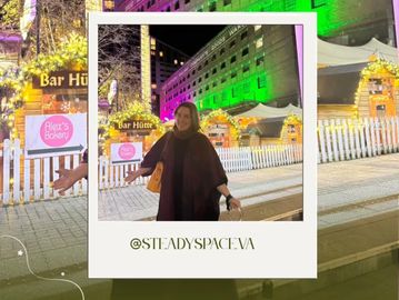 Woman smiling in front of a brightly lit building and festive market at night.