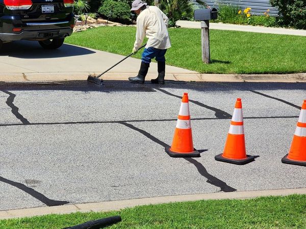 Worker sealing cracks on a suburban street with safety cones nearby.