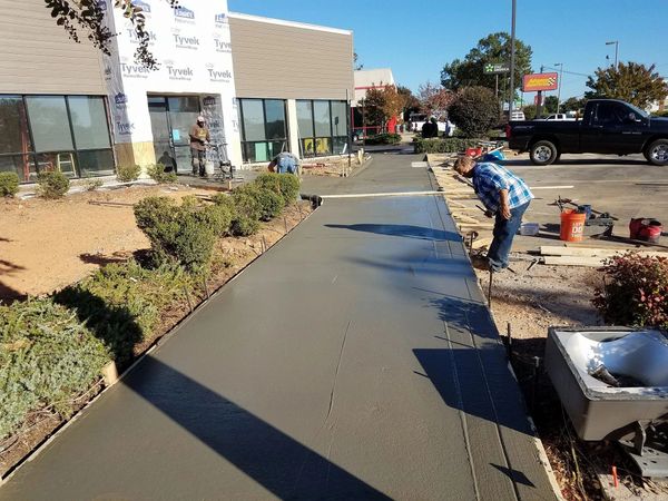 Workers smoothing fresh concrete on a sidewalk outside a building under construction.