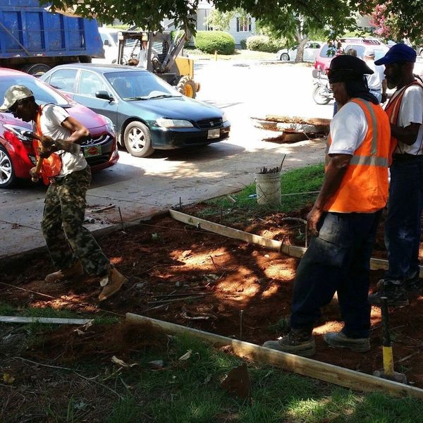 Three construction workers preparing a site near a street with parked cars.