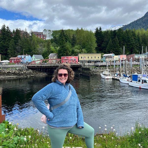 Woman who specializes in planning stress-free travel posing by a waterfront with colorful houses and boats in the background in Alaska .