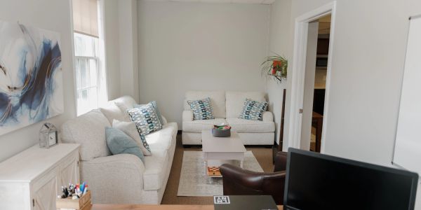 Cozy, well-lit living room with white sofas and decorative cushions.