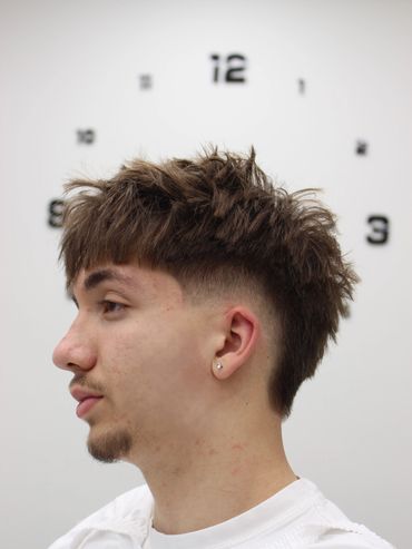 Side profile of a young man with a trendy textured haircut against a clock background.