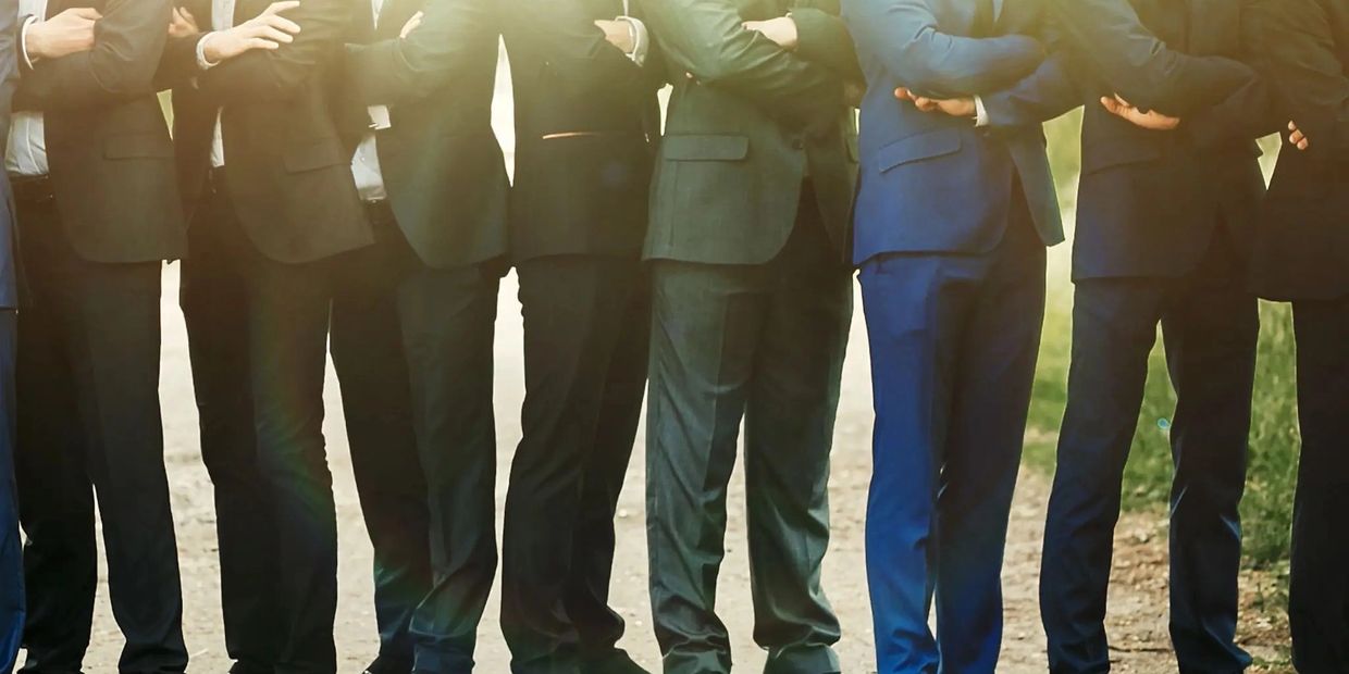 Group of men in suits standing with crossed arms outdoors.