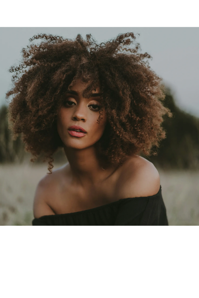 Close-up portrait of a woman with voluminous curly hair and an off-shoulder black top.