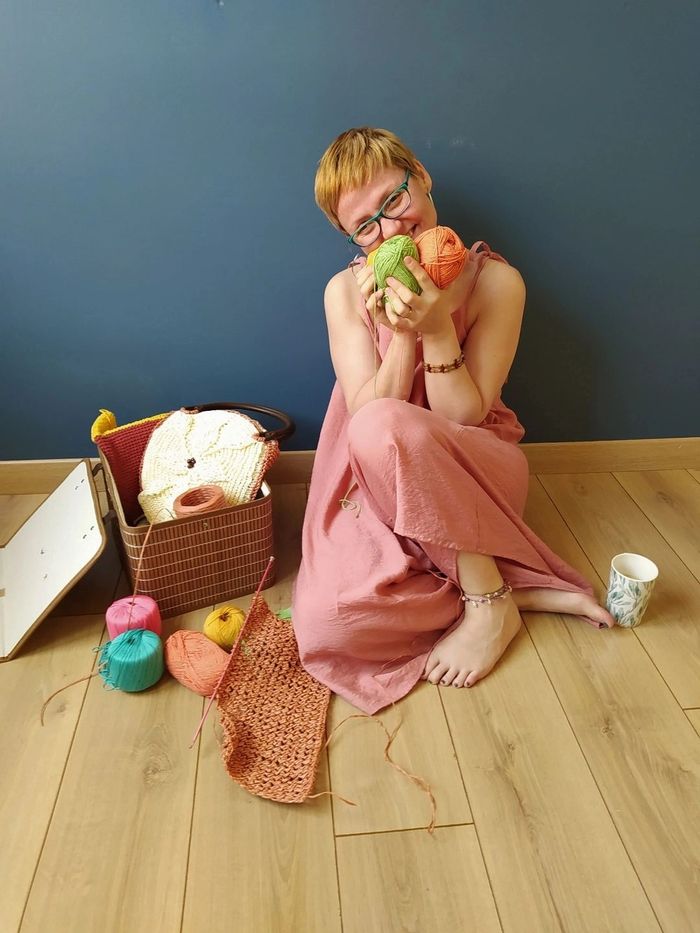 Crochet artist holding yarn balls, surrounded by handmade crochet items and colorful yarn