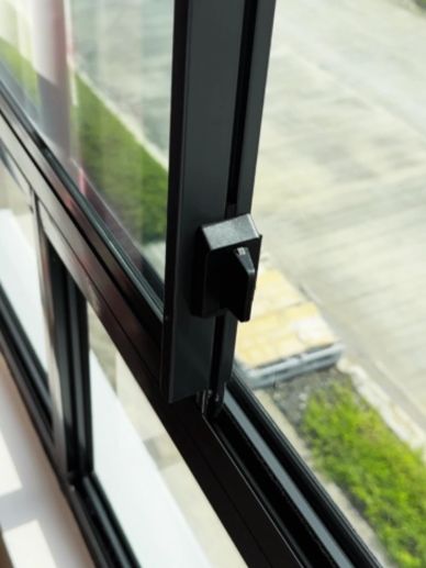 A close-up of a black window latch on a sliding glass window.
