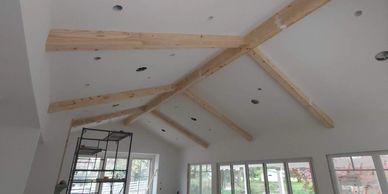 Room under construction with exposed wooden beams and large windows.
