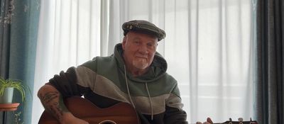 Man wearing a cap playing an acoustic guitar indoors.