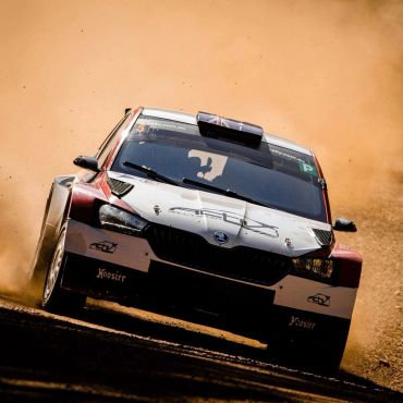 Rally car kicking up dust as it speeds on a dirt track.
