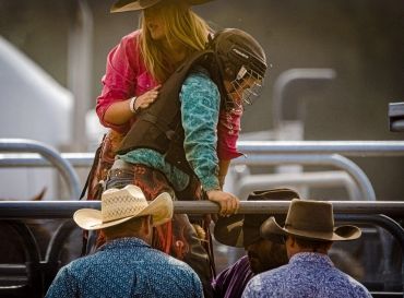 Woman cowboy helping a young rider with helmet and vest.