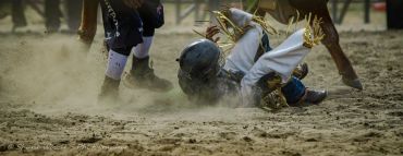 A rodeo participant falls off a bull on a dusty arena ground.