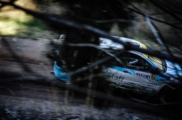 Rally car speeding through a forested dirt path.
