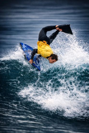 Surfer in a yellow top performs an aerial trick on a wave.