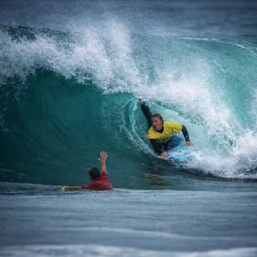 Surfer skillfully riding inside a large curling wave while another person watches from the water.