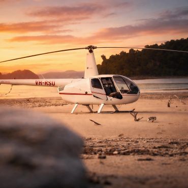 White helicopter on sandy beach during sunset with hills in background.