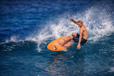Surfer riding a wave on an orange surfboard in the ocean.