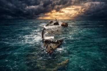 Shipwreck ruins emerging from stormy ocean waters under dramatic skies.