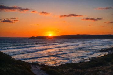 Sunset over a calm ocean with waves rolling to the shore.
