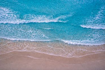 Gentle waves of clear blue ocean meet the sandy shore.