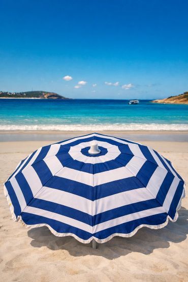 Blue and white striped beach umbrella on a sandy shore with a calm sea.