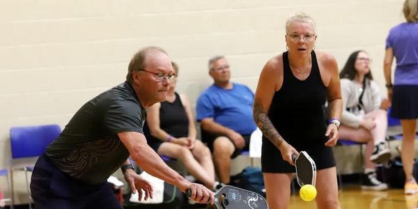 Two adults playing pickleball indoors, focused and active.