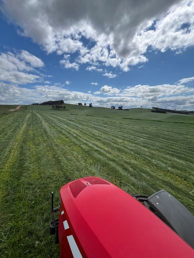 A red tractor in a vast green field under a partly cloudy sky.