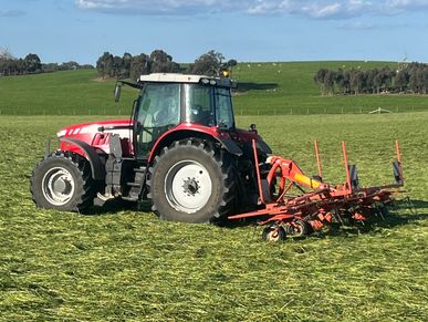 Red tractor with farming equipment on green field under blue sky.