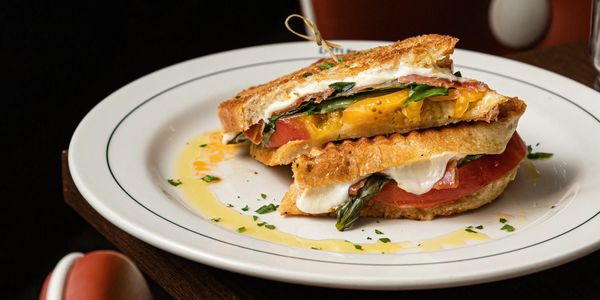 Grilled sandwich with fresh tomatoes, melted cheese, and greens on a white plate.