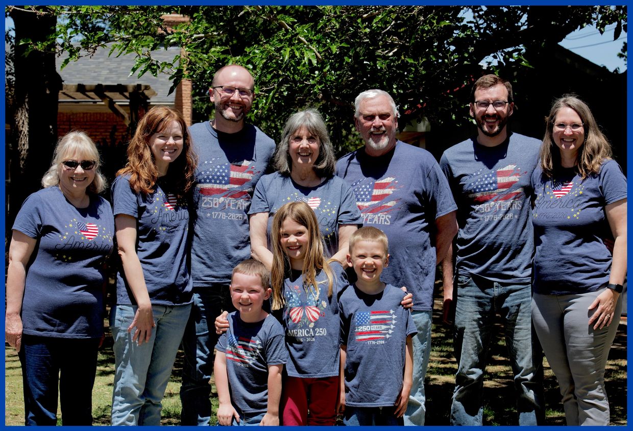 Family group posing outdoors in matching America-themed shirts.