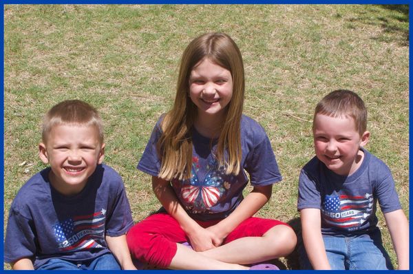 Three kids sitting on grass smiling.