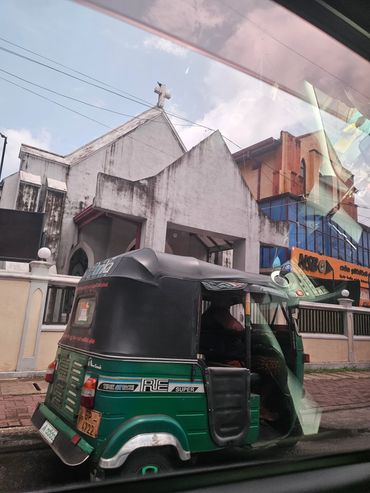 Green and black auto rickshaw near a church building.