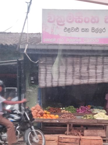Motorcyclist passing by a vegetable shop with various produce.