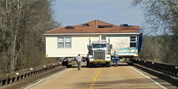 A large truck transports a mobile home on a country road.